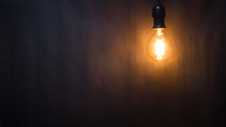 Light bulb hanging in a dark room for National Electrical Safety Awareness Month.